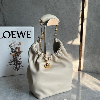 Loewe羅意威 現款Squeeze腋下包包上市啦 這款包以其褶設計感的Hobo造型展現出高級慵懶感和柔和的女性魅力，由Nappa帕羊皮製成，包身柔軟絲滑，光澤閃亮如綢緞，金色圓形小球的點綴，與觸感絲滑的皮革相得益彰 其特色在於甜甜圈形狀的